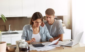 A couple sitting at a kitchen table reviewing papers or using a laptop.