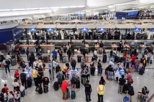 Passengers queue at airline check-in desks while self-service kiosks are unavailable during a system outage
