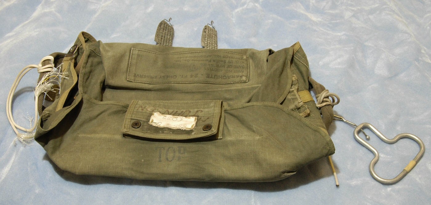 Green military-style parachute pack and red-pink canopy fabric laid out on a table, believed to be linked to the 1971 D.B. Cooper hijacking.