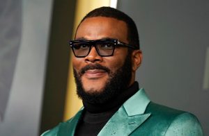 Filmmaker Tyler Perry wearing glasses and a green suit at a red carpet event