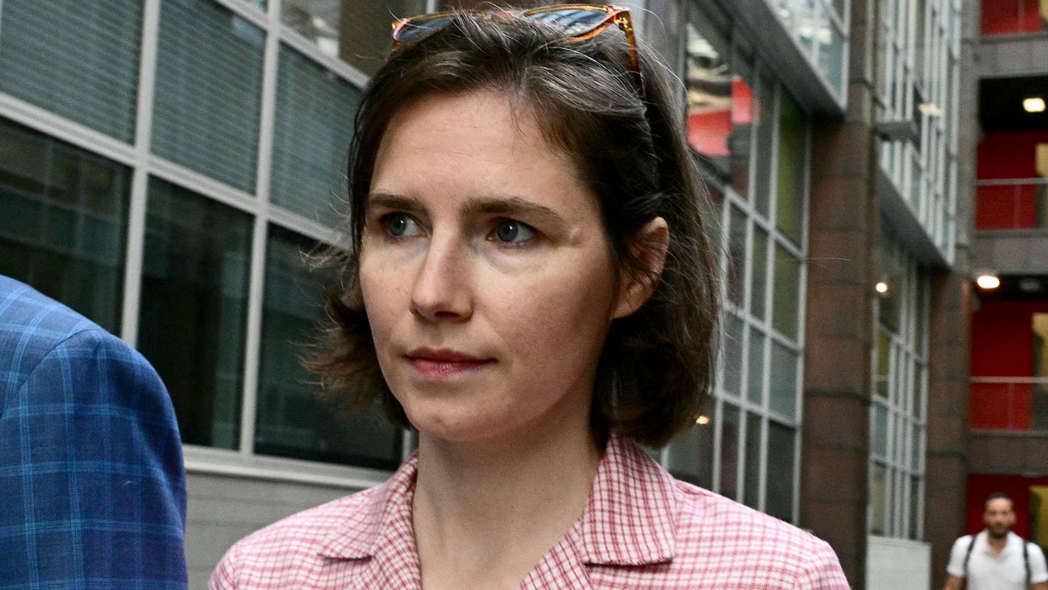 Amanda Knox walking outdoors in an urban setting, wearing a pink checkered shirt, photographed in daylight.