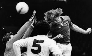 Footballers contest a high ball during a match, illustrating the physical impact of repeated heading.