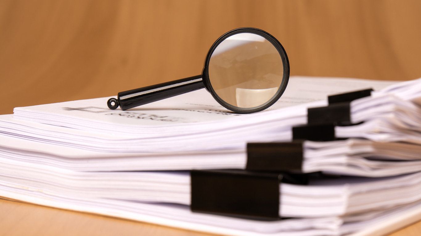 a magnifying glass that is positioned on a stack of papers, which are secured by clips