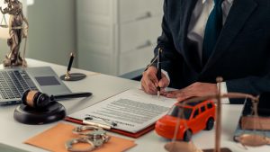a small red toy car sits next to a judge's gavel on a table in a lawyer's office. car accident concept. law. close up of