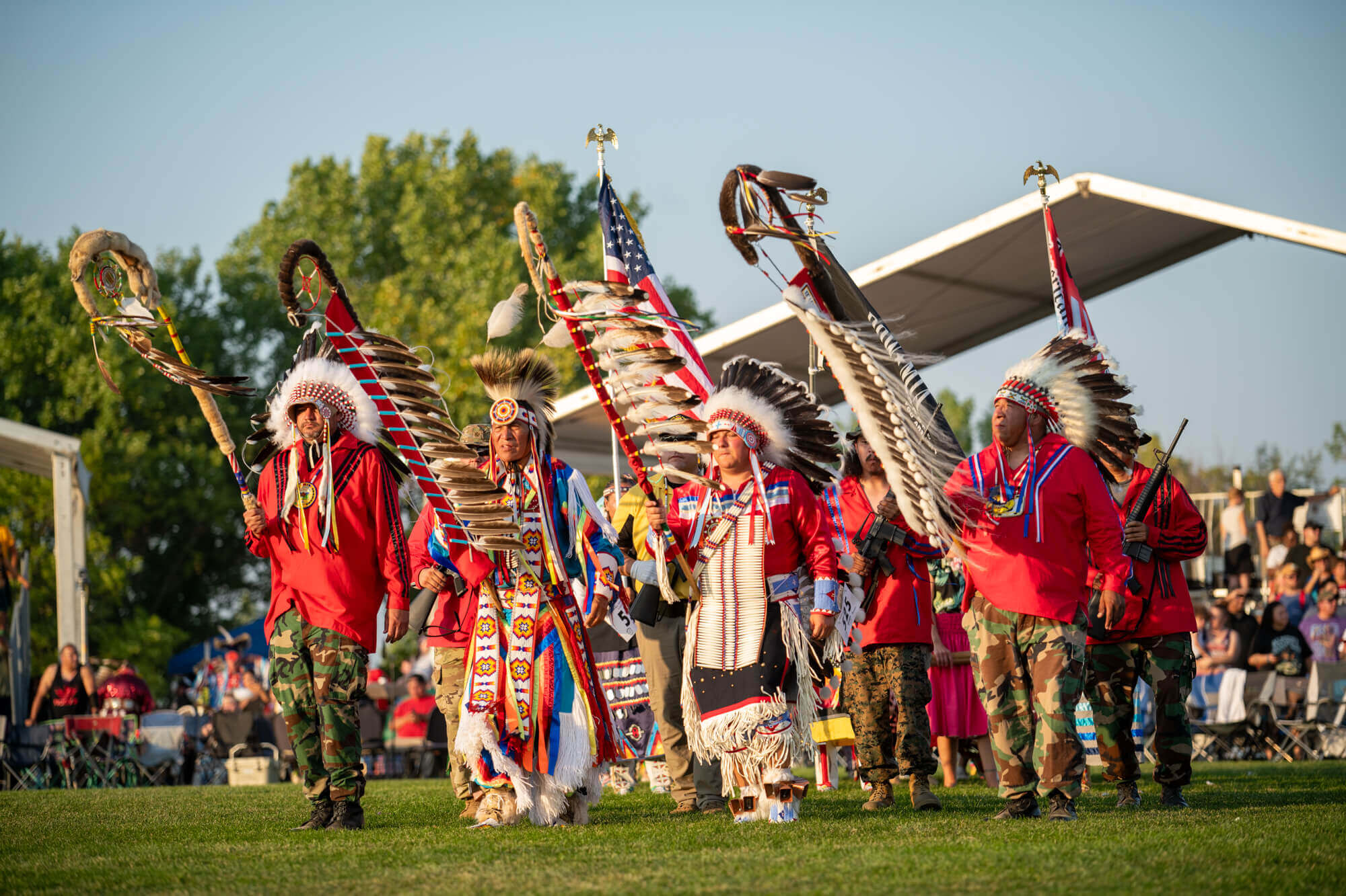 Mdewakanton Dakota Sioux men in traditional regalia during a ceremonial gathering, carrying eagle staffs and flags at a powwow in Minnesota.