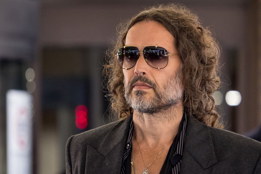 Russell Brand arriving for a court appearance wearing sunglasses and a dark jacket