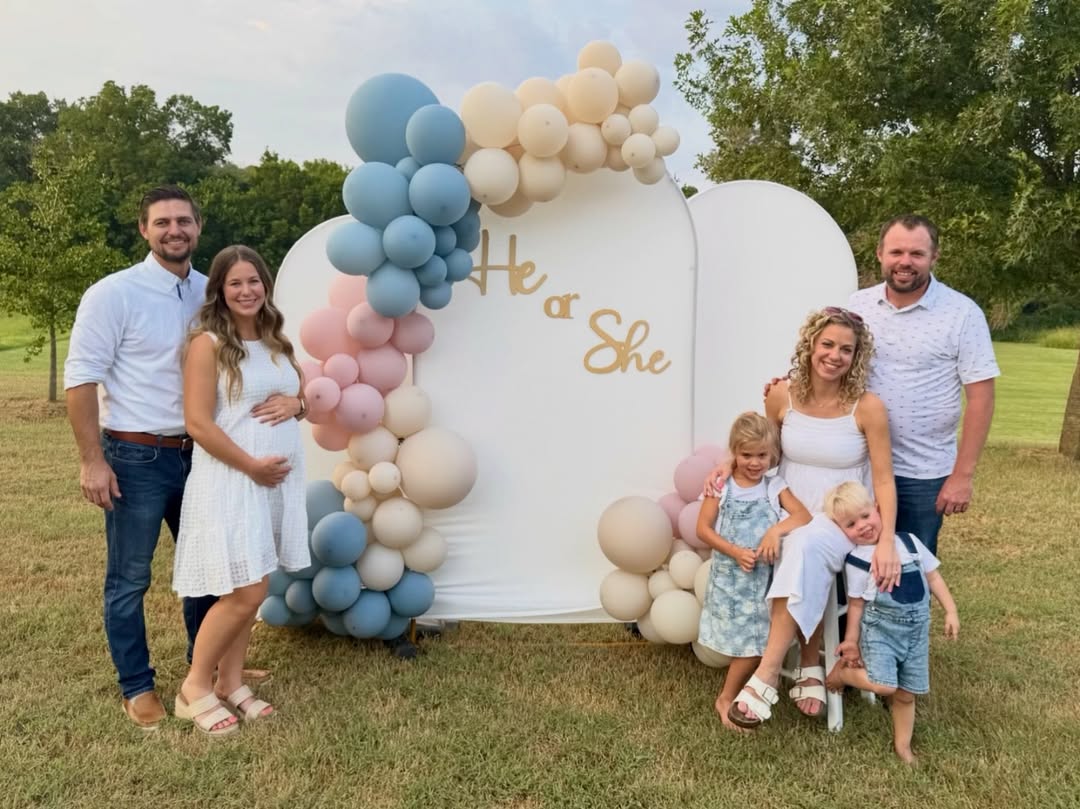 Jana and John-David Duggar with their spouses and children at a joint gender reveal party featuring a &ldquo;He or She&rdquo; balloon display outdoors.