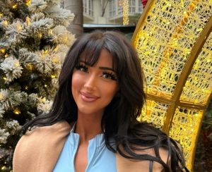 Nala Ray standing outdoors in front of holiday decorations, wearing a light blue zip-front top and tan coat.