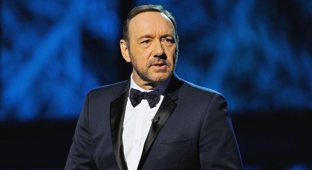 Kevin Spacey speaking on stage in a tuxedo at a formal event
